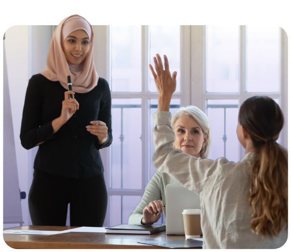 Three women in meeting room with one raising her hand